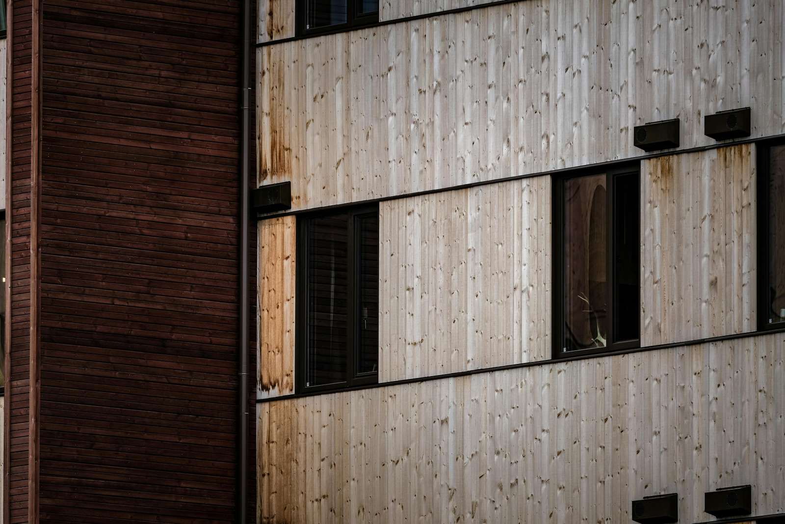 Facade med lodret, gråt og vejrbidt træbeklædning og mørke vinduer