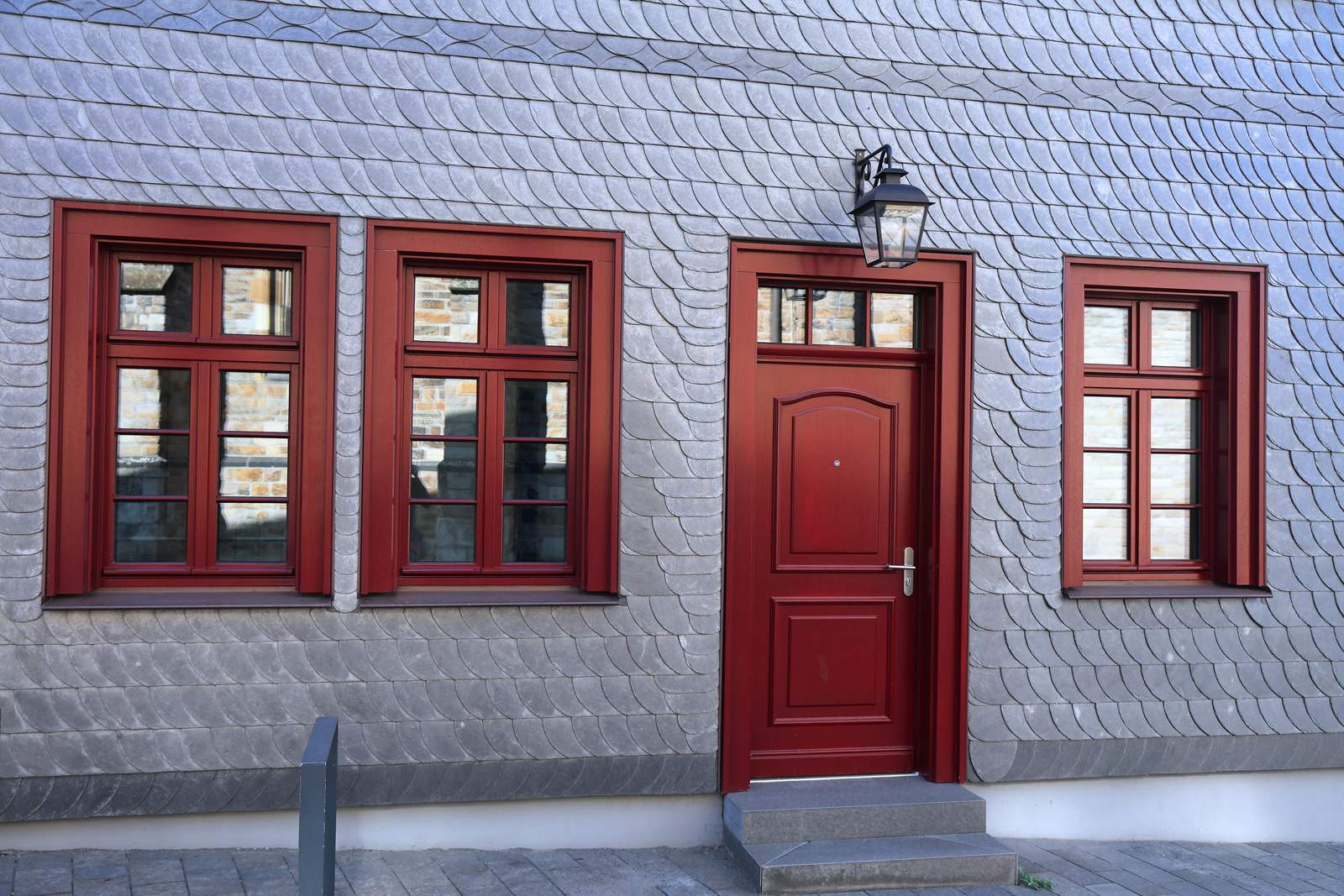 Facade beklædt med grå skiferplader og røde vinduer og dør