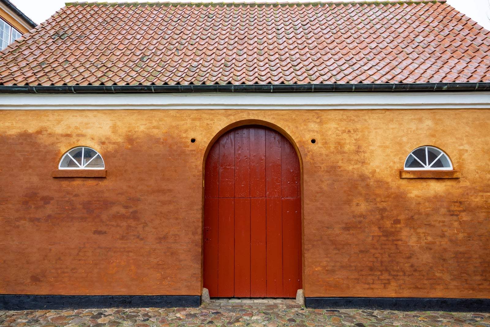 Okkergul pudset facade med rød buet port og tegltag